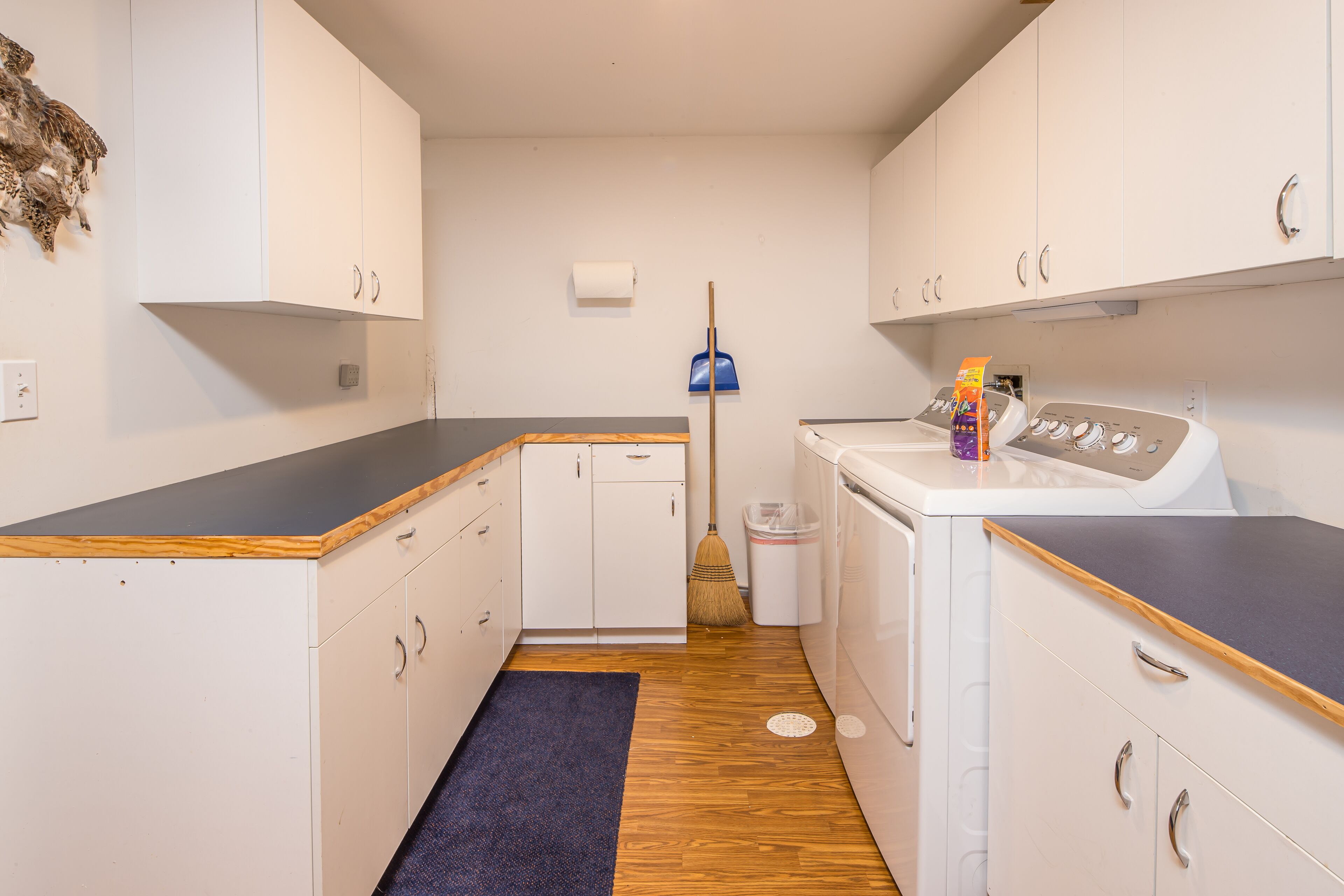 A compact kitchen with white cabinets, a wooden countertop, a washing machine, and a broom.