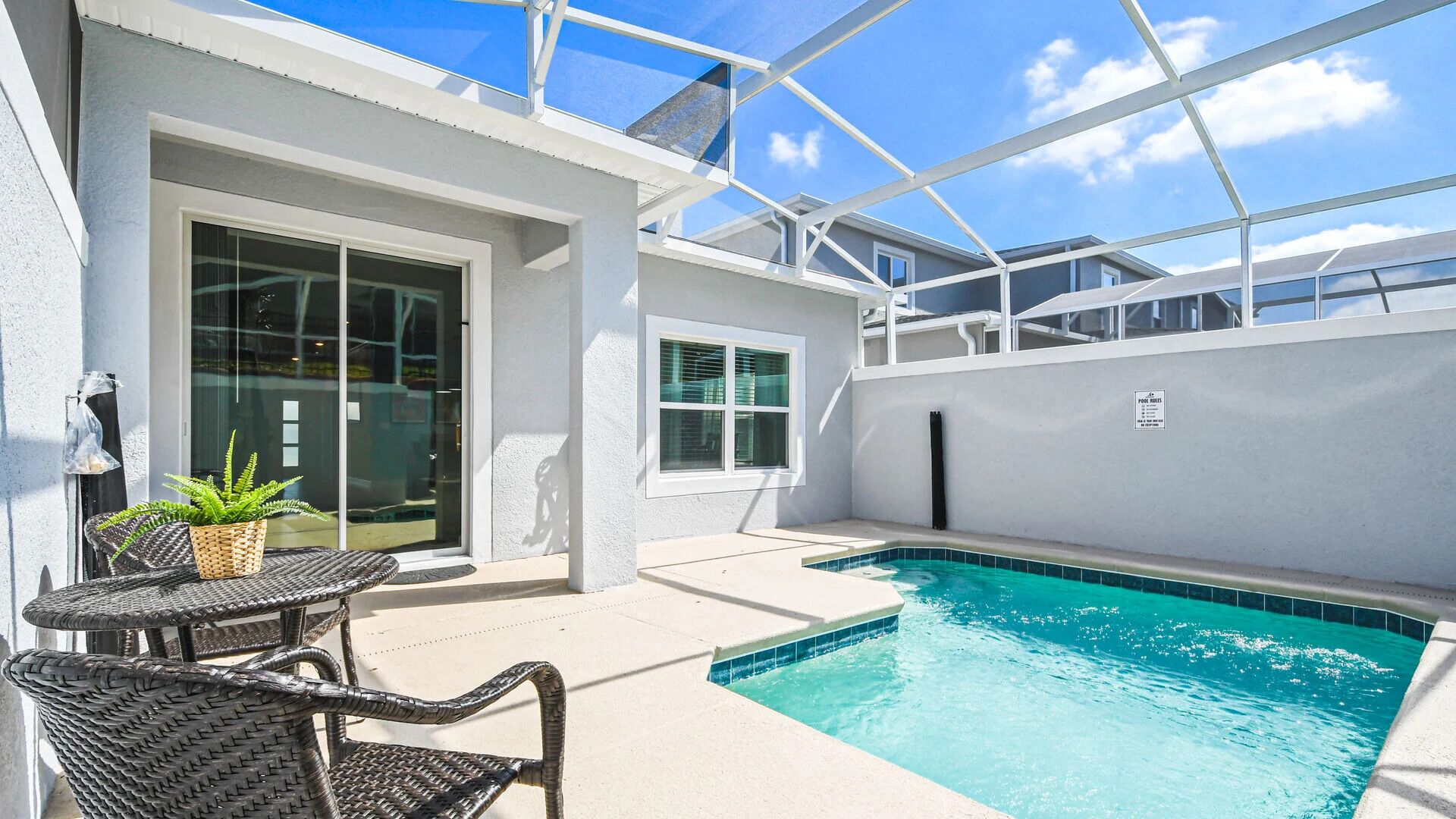 A pool area with a glass-enclosed structure, a seating area with a table and chairs, and a sign indicating pool rules.