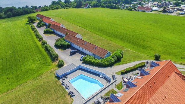 Vista aerea di una proprietà con piscina, un ampio prato verde e una distesa d'acqua sullo sfondo.