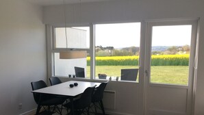 Un'area pranzo con tavolo e sedie, ampie finestre vista su un campo e un tappeto bianco e nero.