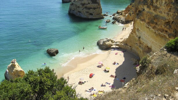 A coastal beach with clear turquoise waters, rocky cliffs, and a sandy shore with umbrellas and people. - Sunny Beach Diamond by Interhome (Armação de Pêra)