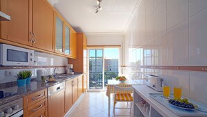 A modern kitchen with wooden cabinets, a microwave, and a coffee maker. There is a dining area with a table and chairs, and a balcony with a view of buildings. - Sunny Beach Diamond by Interhome (Armação de Pêra)