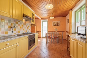 A kitchen with yellow cabinets, a tiled backsplash, a stove, and a dining area with chairs and a table.