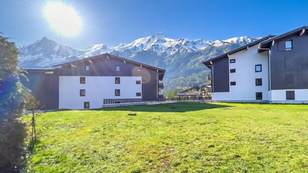 Un edificio moderno con techo plano, un área pequeña cercada y montañas al fondo.