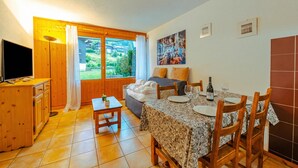 A cozy room with a bed, a dining table with chairs, a TV, and a window with curtains. - Le Prarion RDC Ski in/Ski out at Les Houches (Sleeps 4), Les Houches (Chamonix), France (Les Houches (Chamonix))