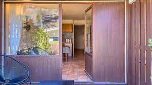 Una habitación con puerta corredera que da a una cocina, un comedor con mesa y sillas, y vistas a través de una ventana con cortinas.