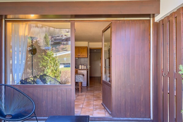 A room with a sliding door leading to a kitchen, a dining area with a table and chairs, and a view through a window with curtains. - Résidence Le Prarion RDC ski in/ski out, Les Houches (Chamonix), France (Les Houches (Chamonix))