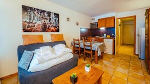 A cozy living room with a sofa, a dining table, and a kitchen area with cabinets and a microwave. - Le Prarion RDC Ski in/Ski out at Les Houches (Sleeps 4), Les Houches (Chamonix), France (Les Houches (Chamonix))