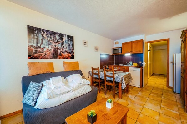 A cozy living room with a sofa, a dining table, and a kitchen area with cabinets and a microwave. - Le Prarion RDC Ski in/Ski out at Les Houches (Sleeps 4), Les Houches (Chamonix), France (Les Houches (Chamonix))