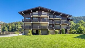 A multi-story building with balconies, a flat roof, and a grassy foreground. - Le Prarion RDC Ski in/Ski out at Les Houches (Sleeps 4), Les Houches (Chamonix), France (Les Houches (Chamonix))