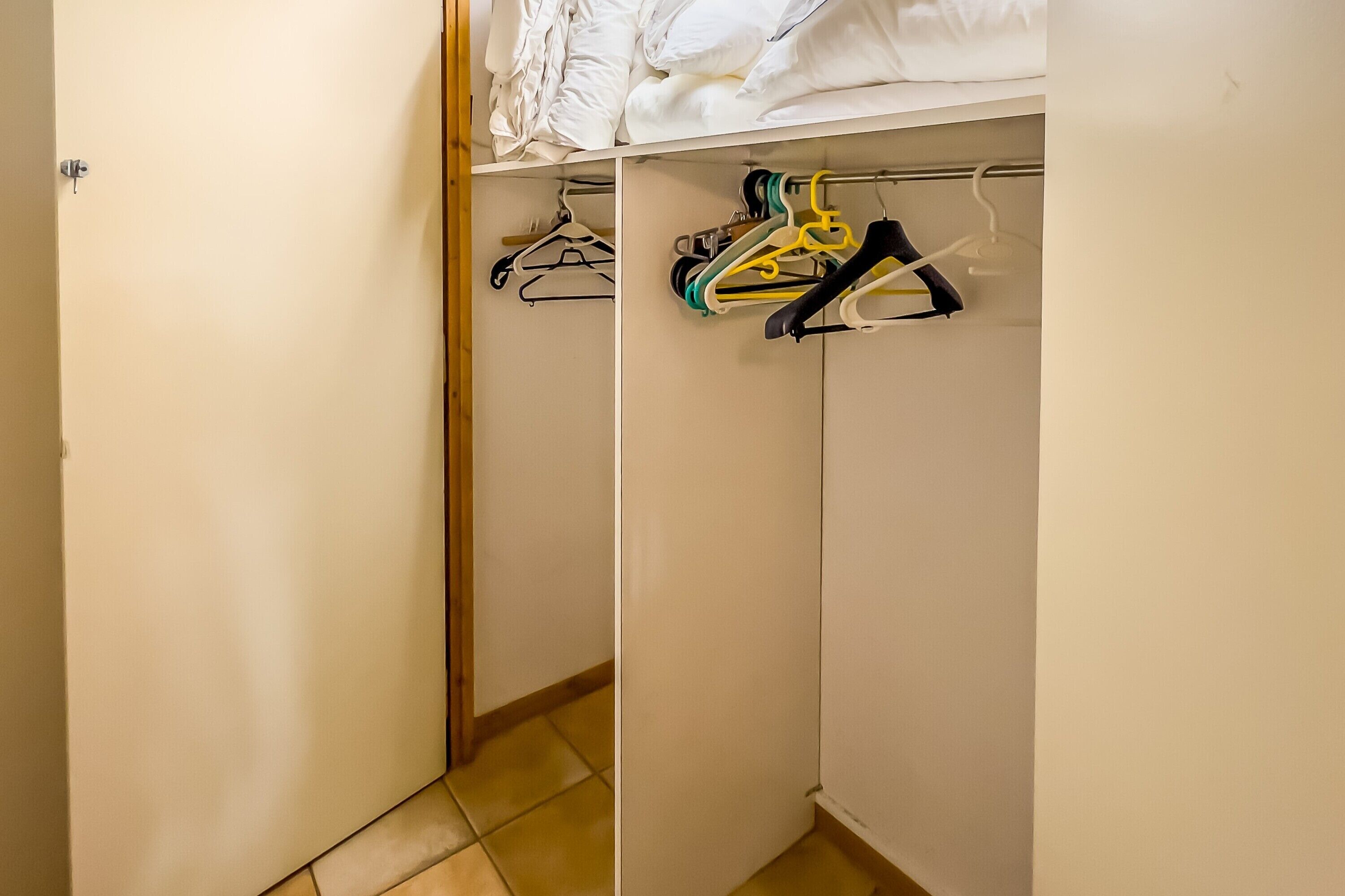 Ein begehbarer Kleiderschrank mit weißen Wänden, einer Holztür und Fliesenboden.