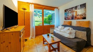 A room with a TV, wooden furniture, a sofa, a table with plants, and a painting on the wall. - Le Prarion RDC Ski in/Ski out at Les Houches (Sleeps 4), Les Houches (Chamonix), France (Les Houches (Chamonix))