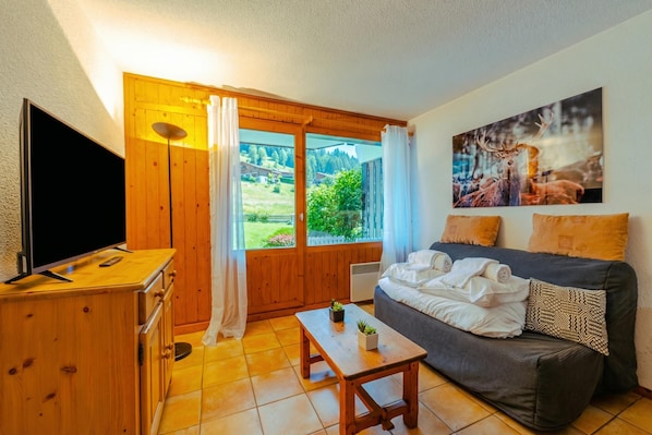 Una habitación con televisión, muebles de madera, un sofá, una mesa con plantas y un cuadro en la pared.