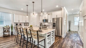 A modern kitchen with white cabinetry, a central island with bar stools, stainless steel appliances, and pendant lighting. - Beach, Private Pool, Designer Everything, Exclusive  Community (Hilton Head Island)