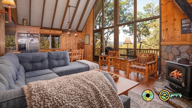 A cozy cabin interior with a large sofa, wooden furniture, a stone fireplace, and a view of the outdoors. - Holocene Chalet - treetop mountain views! (Basye)
