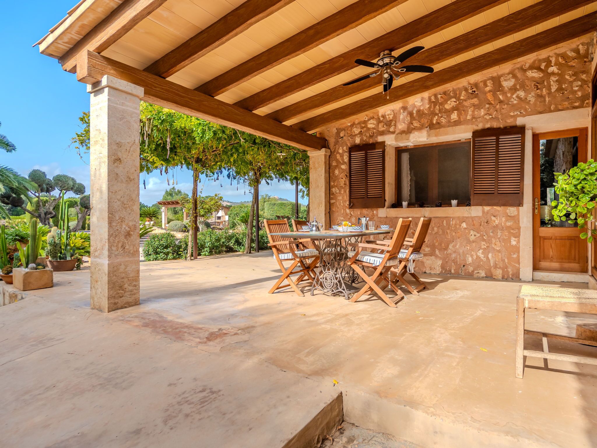 A covered patio with a table and chairs, a ceiling fan, and a stone wall.