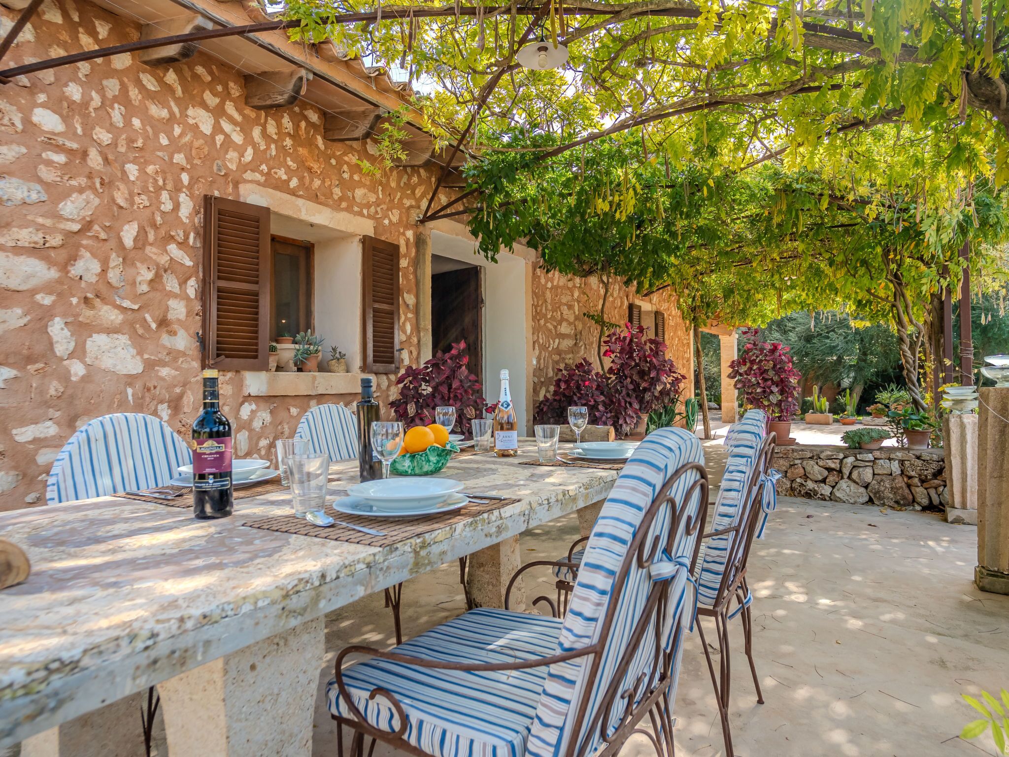 An outdoor dining area with a stone wall, striped chairs, and a table set for two.