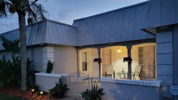 A modern house with a covered porch, a dining area with a table and chairs, and a small garden with plants and a pathway. - Beautiful pool house in Holiday, Florida.  (Holiday)