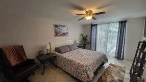 A bedroom with a bed, a desk, a chair, a ceiling fan, a window with curtains, and a painting on the wall. - Beautiful pool house in Holiday, Florida.  (Holiday)