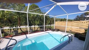 A covered outdoor swimming pool with a clear view of the surrounding greenery and a wooden fence. - Beautiful pool house in Holiday, Florida.  (Holiday)