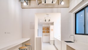 Una cocina moderna con armarios blancos, un ventanal y un estante empotrado con cestas. Hay tres taburetes con asientos de madera.