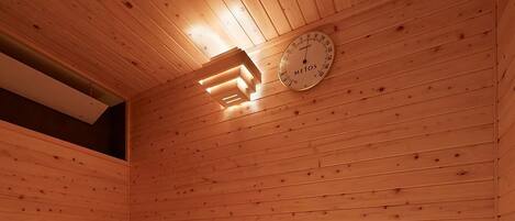Una sauna de madera con bancos y un termómetro colgado en la pared.
