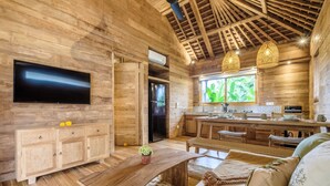 A wooden interior with a TV, dining area, kitchen, and seating. - Kaju Bungalow by Betterplace (Canggu)