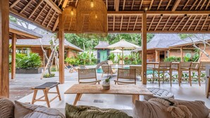 An outdoor seating area with wooden furniture, a table, and hanging lights. - Kaju Bungalow by Betterplace (Canggu)
