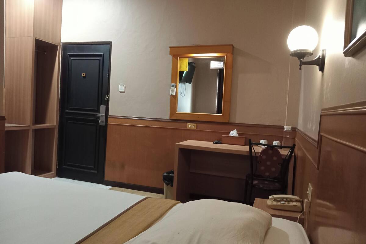 Une chambre d’hôtel avec un lit, un bureau, une chaise, un miroir et un téléphone.