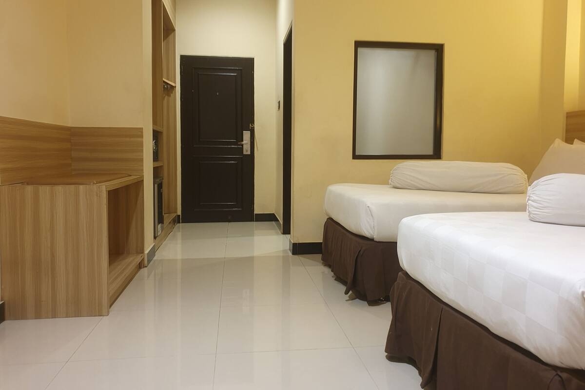 Une chambre d’hôtel avec une armoire en bois, une porte noire, un lit avec du linge de lit blanc et un miroir fixé au mur.