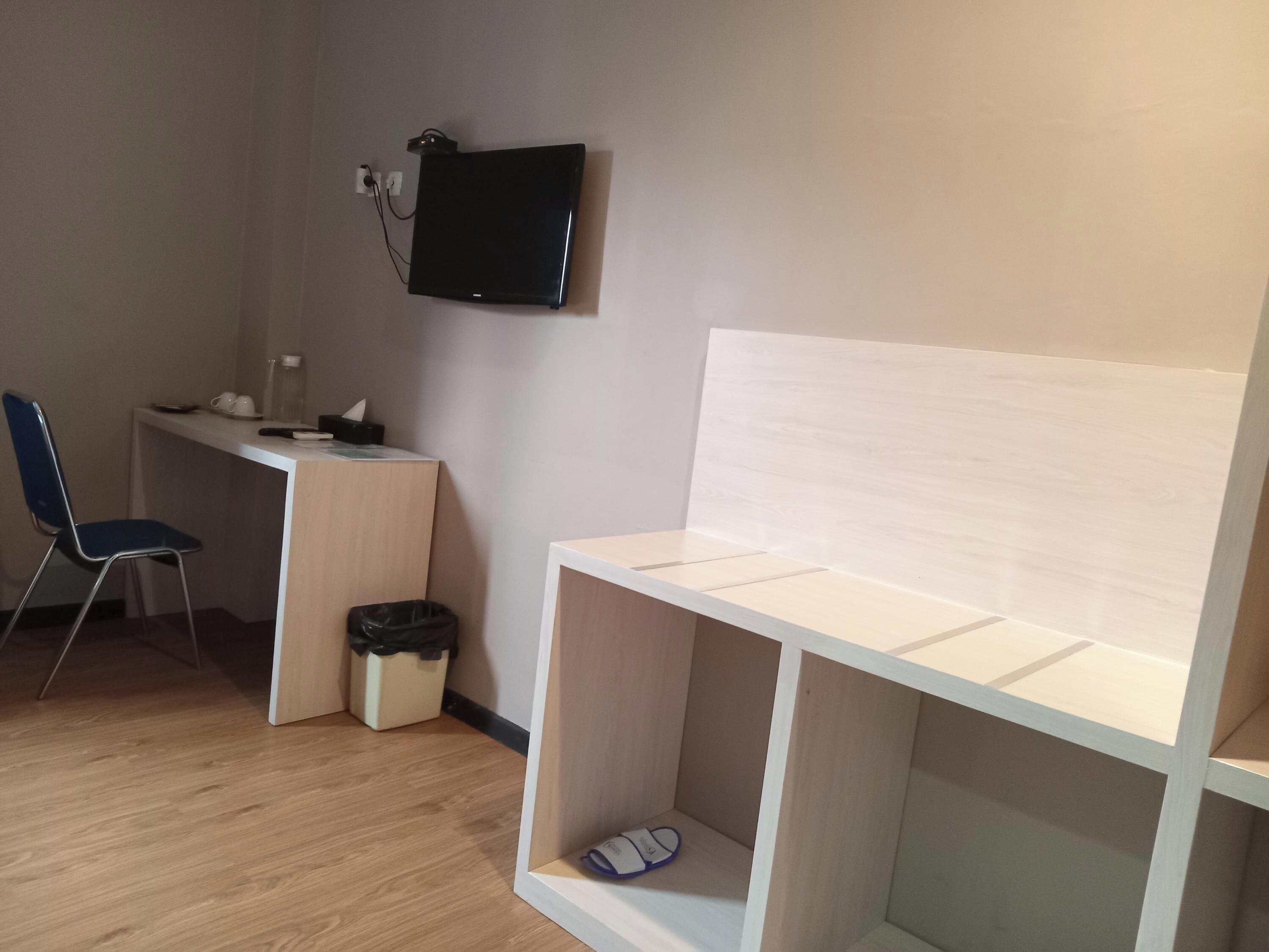 Ein Zimmer mit Holzboden, einem weißen Schreibtisch, einem blauen Stuhl, einer schwarzen Mülleimer und einem weißen Regal.