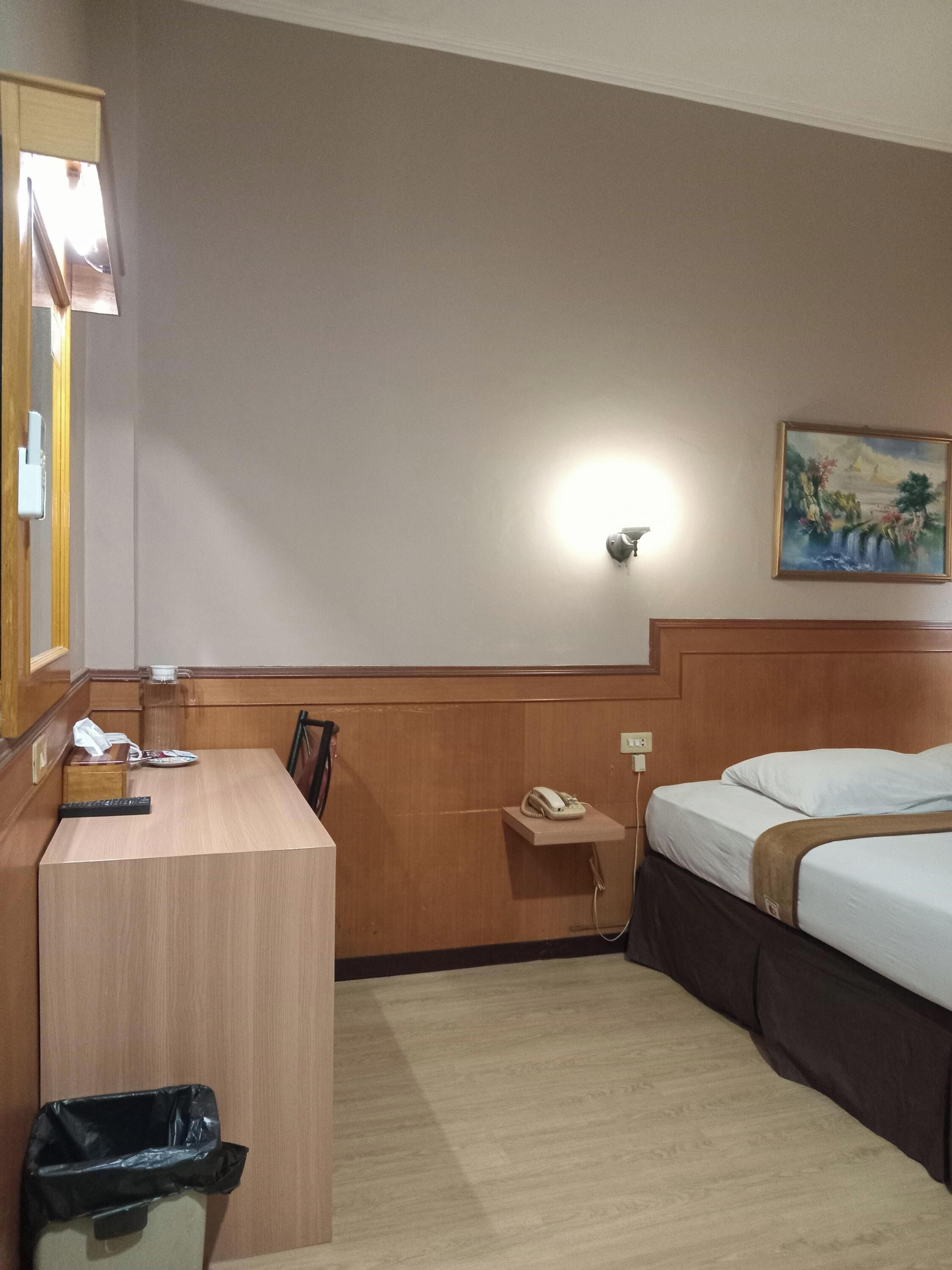 Une chambre d’hôtel avec un bureau en bois, un téléphone, une poubelle, un lit et un tableau au mur.