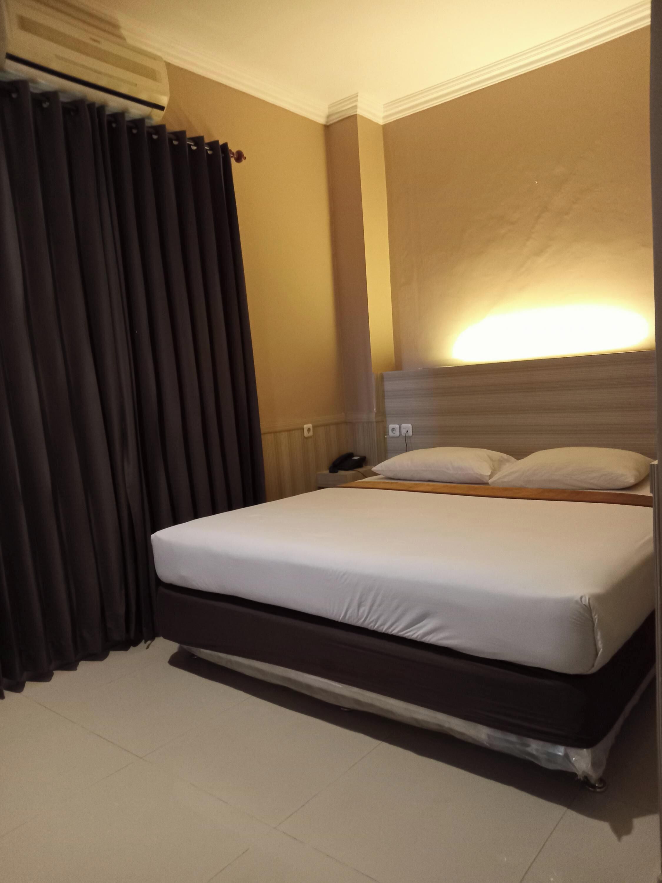 Hotellihuone, jossa on yksi sänky, yöpöydällä puhelin ja seinään kiinnitetty valaisin.