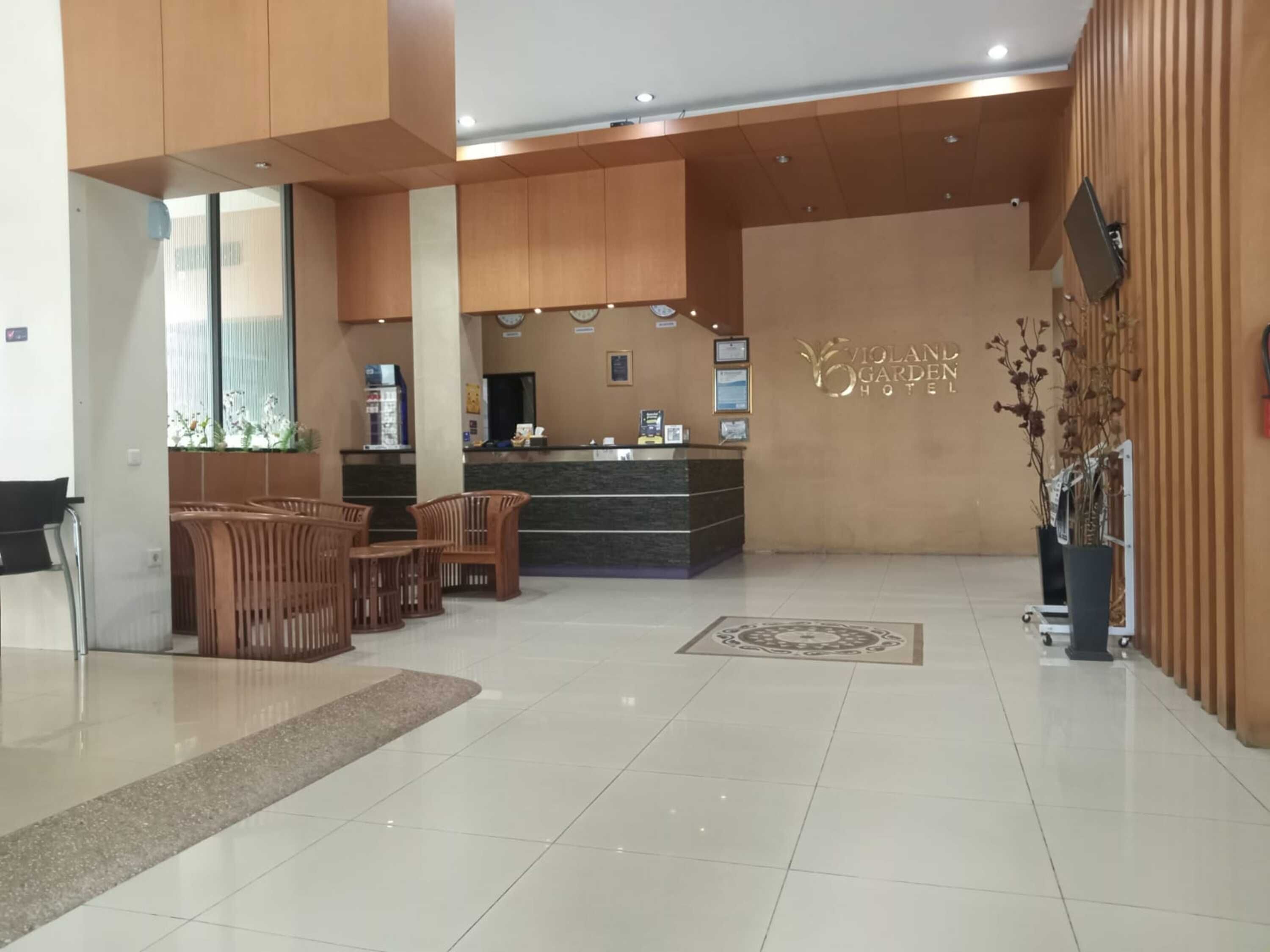 Vestíbulo de hotel con mostrador de recepción, sillas de madera, suelo de baldosas y una pared con el nombre del hotel.