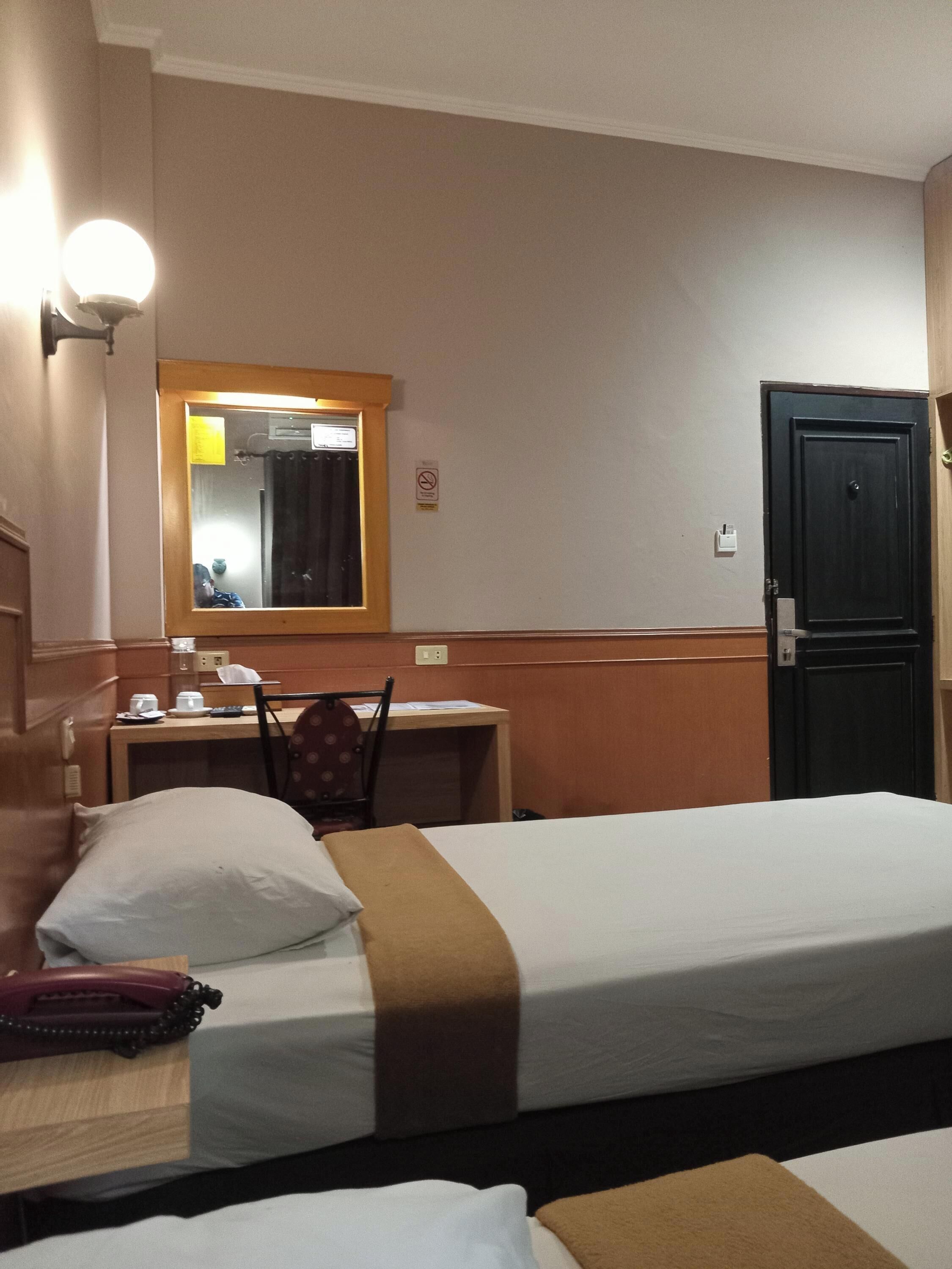 A hotel room with two beds, a desk, a chair, a mirror, and a door.