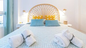 A neatly made bed with a patterned bedspread, two pillows, and rolled towels on a headboard with a circular design. - Palamós: Playa, Sol y Parking incluido (Palamos)