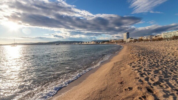 A beach with a clear sky and calm sea, a sandy shore, and buildings in the background. - Palamós: Playa, Sol y Parking incluido (Palamos)