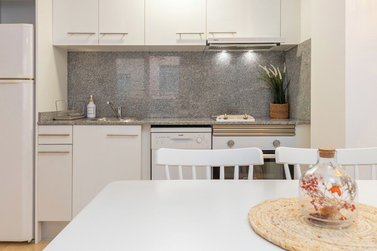 Cocina moderna con armarios blancos, encimera de granito y lavavajillas.