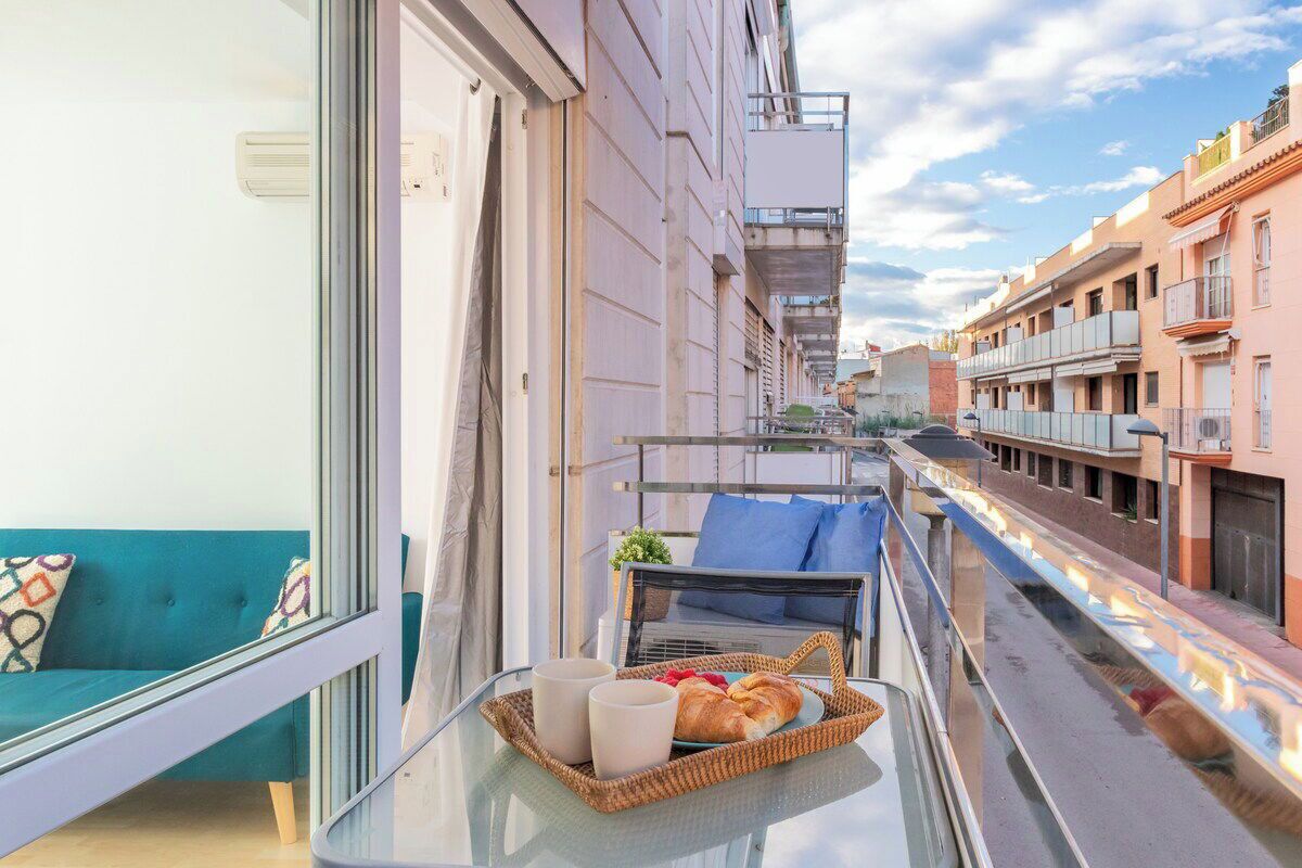 Ein Balkon mit einem Glastisch, einem Korbwannen-Korb mit einem Croissant und einem blauen Sofa.