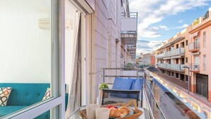 A balcony with a glass table, a wicker basket with a croissant, and a blue sofa. - Palamós: Playa, Sol y Parking incluido (Palamos)