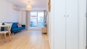A room with a blue sofa, a dining table with chairs, a hanging light fixture, and a view through a window. - Palamós: Playa, Sol y Parking incluido (Palamos)