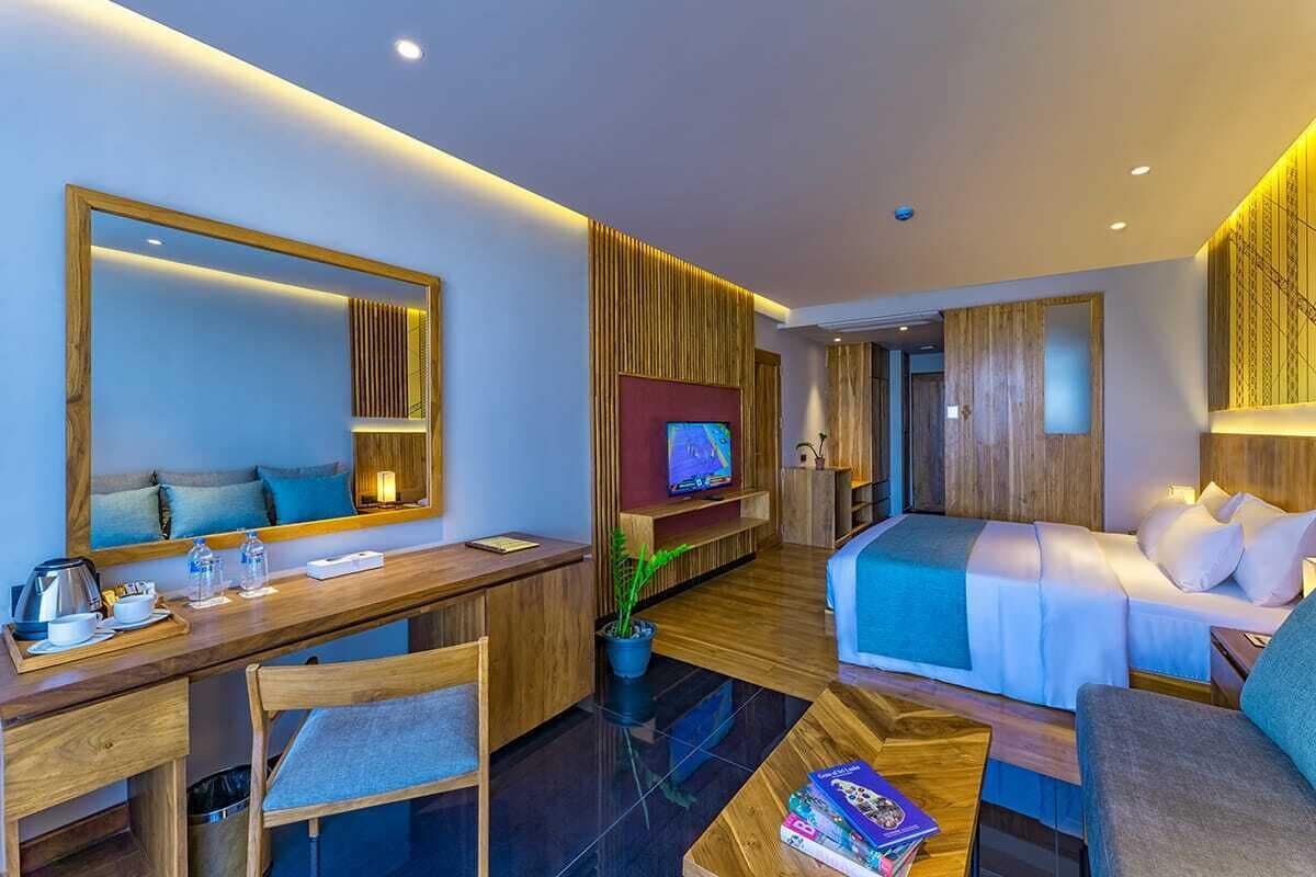 A modern hotel room with a wooden desk, a comfortable sofa, a bed, a TV, and a large mirror.