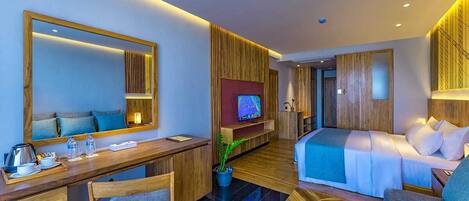 A modern hotel room with a wooden desk, a comfortable sofa, a bed, a TV, and a large mirror.