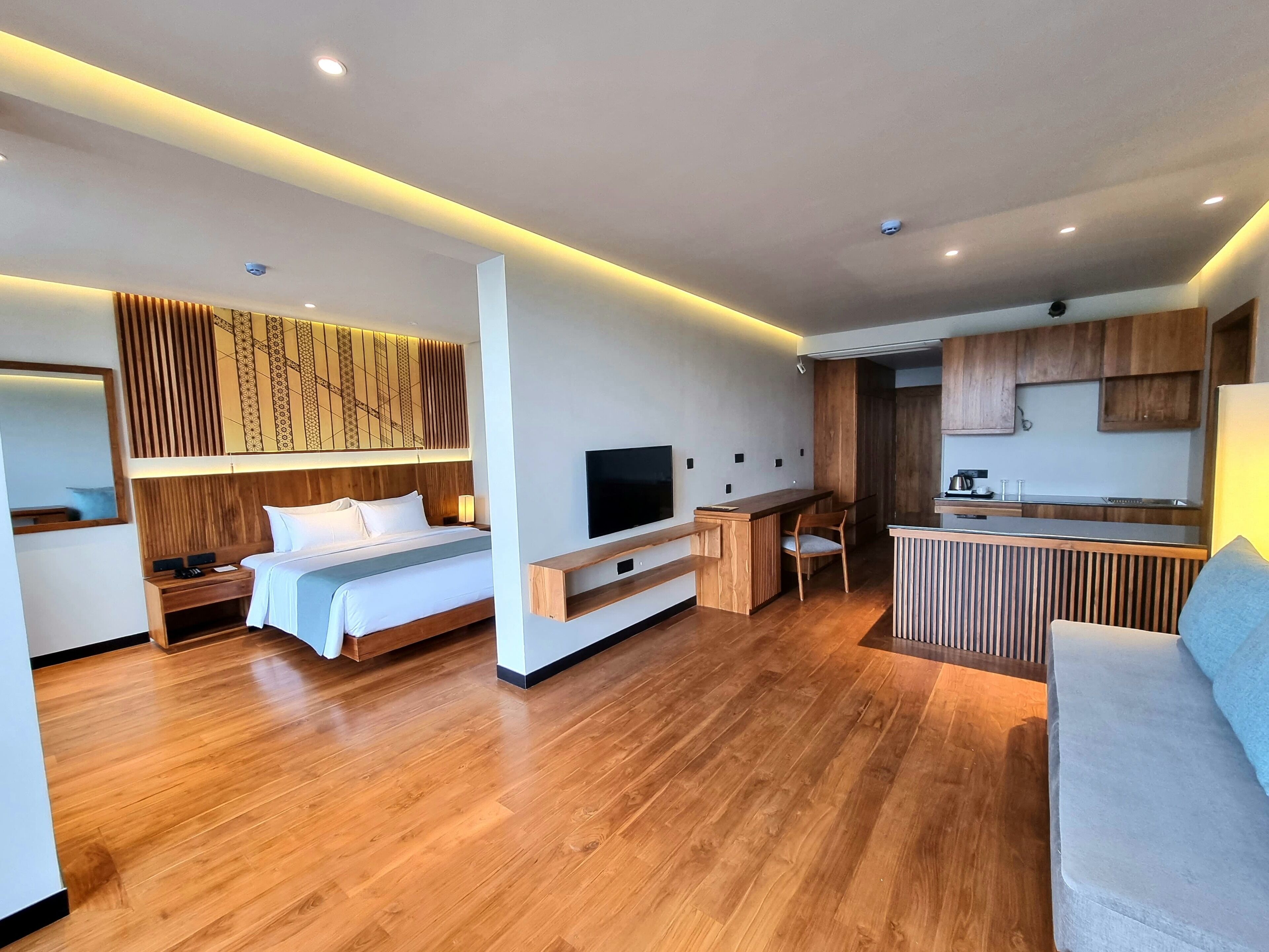 Habitació d'hotel moderna amb terra de fusta, un llit, un televisor, escriptori i una cuineta.