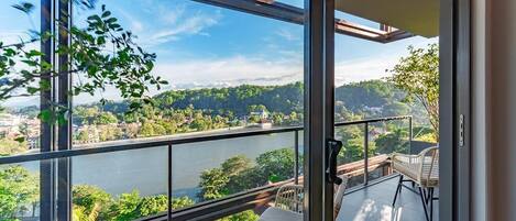 A balcony with a view of a river and hills, wicker furniture, and a glass door.