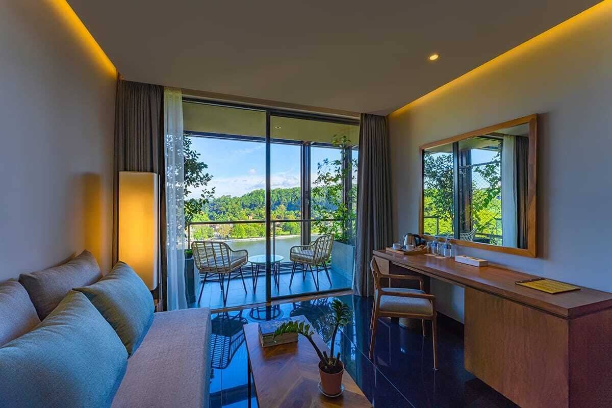 Une chambre d’hôtel moderne dotée d’un grand balcon, d’un canapé, d’une table à manger et d’un bureau avec des chaises.