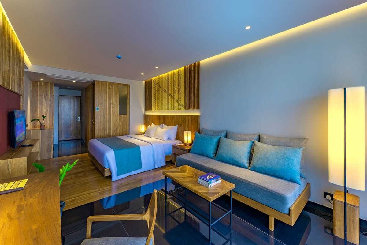 A modern hotel room with a bed, sofa, and a desk with a lamp.