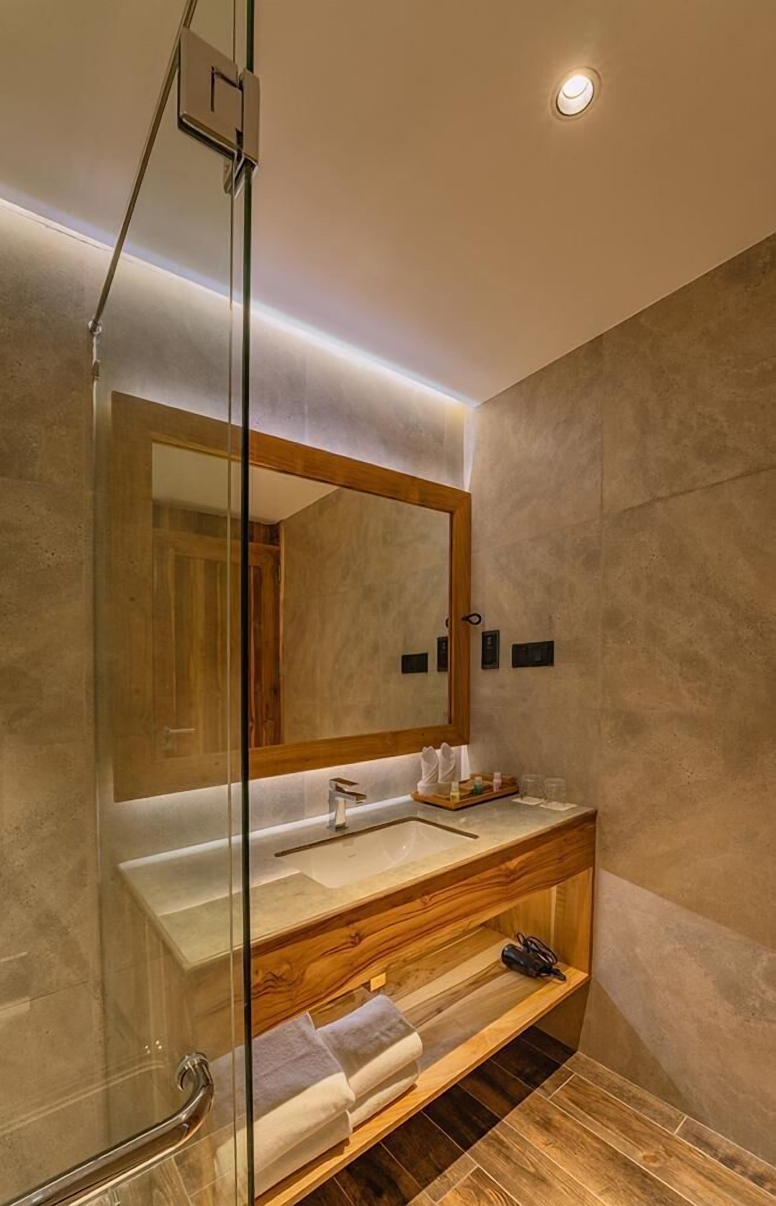 A modern bathroom with a glass shower enclosure, a large mirror, and a wooden vanity with a sink.