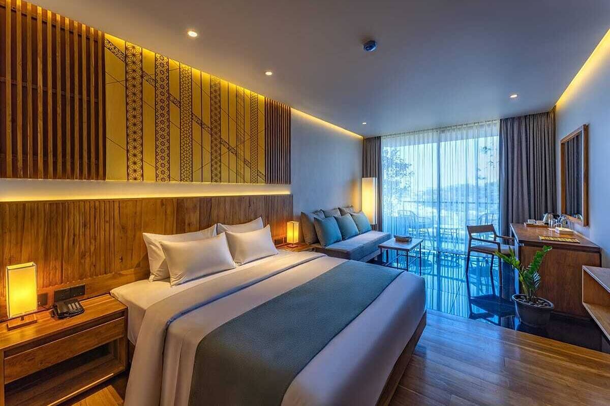 A modern hotel room with a large bed, a sofa, a desk, and a balcony with a view.