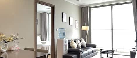 A modern living room with a dining area, a water dispenser, a sofa with cushions, and a large window providing natural light.